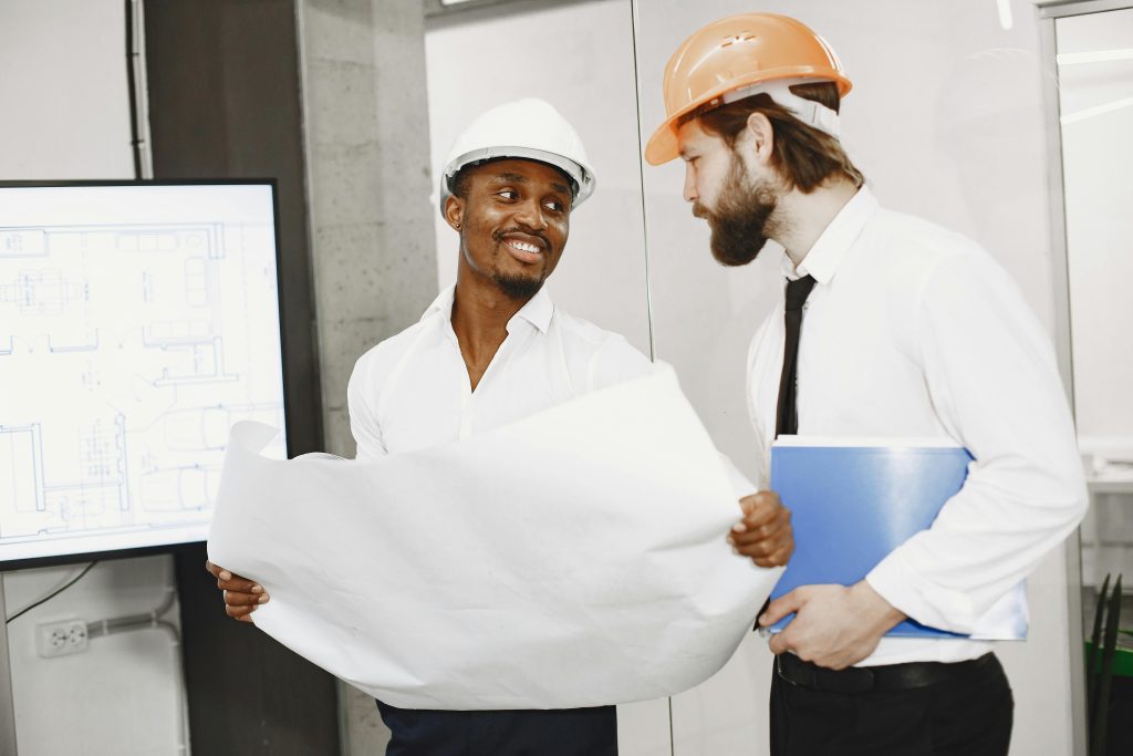 Deux architectes en casques de chantier discutent de plans dans un bureau moderne, mettant en avant le travail d'équipe et la planification.