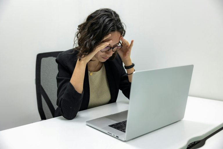 Une jeune femme ressentant du stress et de la fatigue tout en travaillant sur son ordinateur portable dans un bureau.