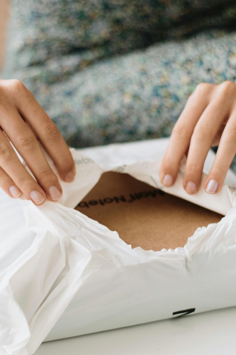 Close-up of hands carefully opening a package, revealing cardboard inside. Gros plan sur les mains ouvrant soigneusement un colis, révélant du carton à l'intérieur.