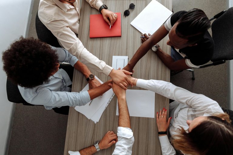 Overhead view of a diverse team placing hands together in a sign of unity during a meeting. Vue de dessus d'une équipe diversifiée plaçant les mains ensemble en signe d'unité lors d'une réunion.