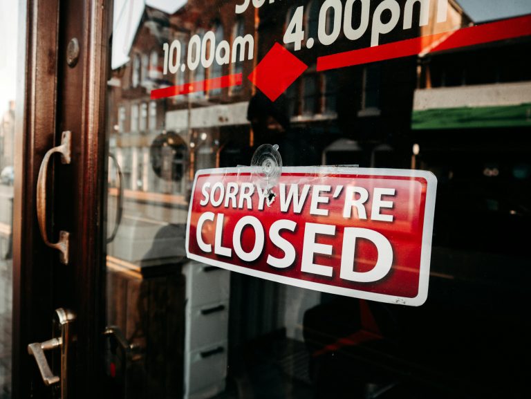 Close-up of a shop's closed sign on a glass door reflecting the street outside. Gros plan d'une pancarte fermée d'une boutique sur une porte vitrée reflétant la rue à l'extérieur.