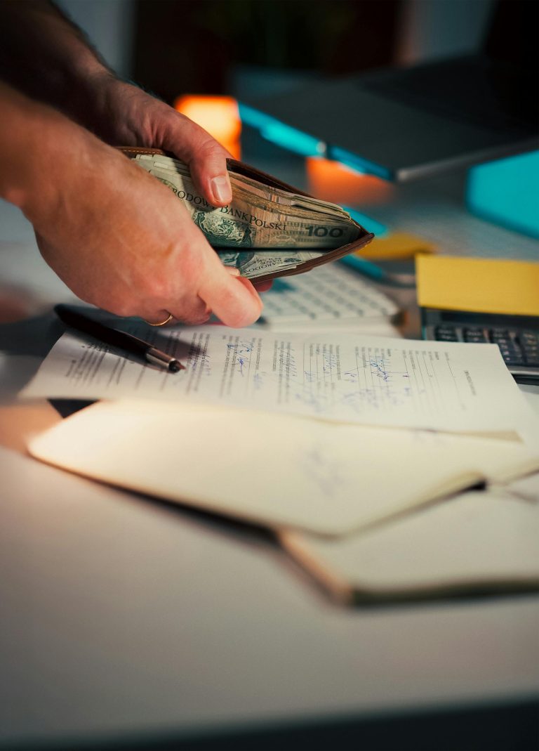 Person handling cash with documents and pen on a desk, suggesting financial management. Personne manipulant des espèces avec des documents et un stylo sur un bureau, suggérant une gestion financière.