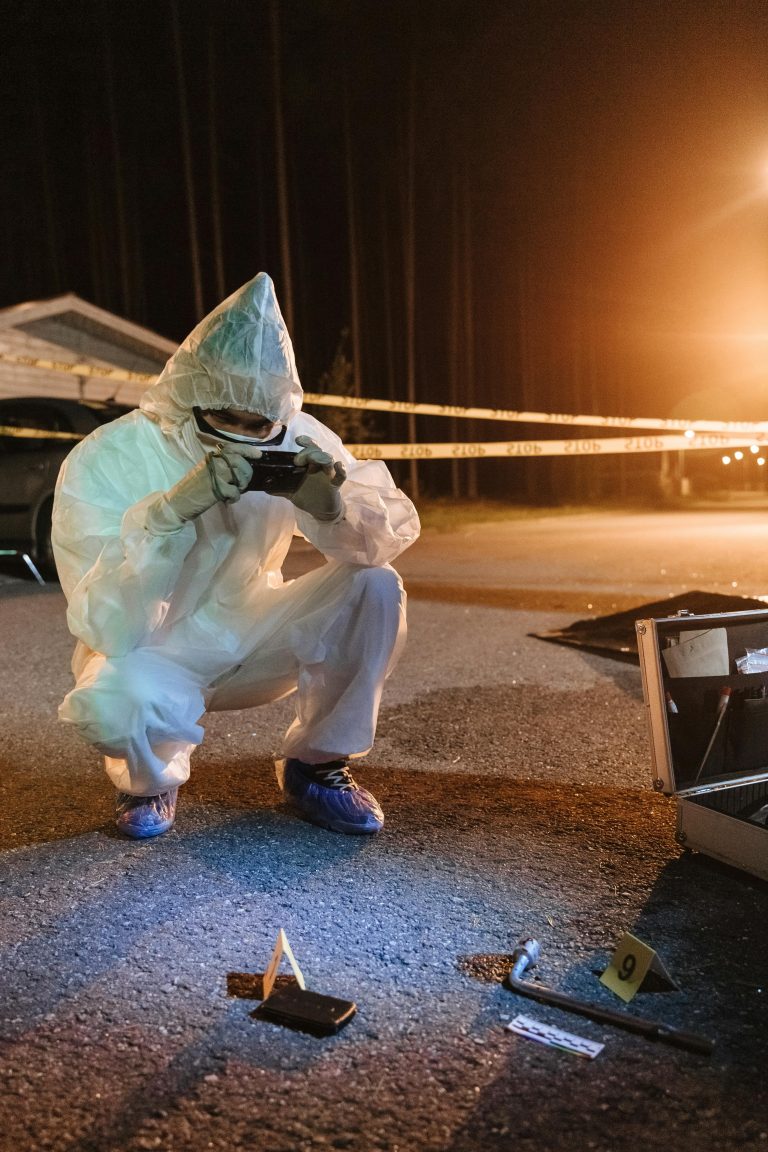 Investigator in protective gear photographing evidence at a night crime scene. Enquêteur en équipement de protection photographiant des preuves sur une scène de crime nocturne.