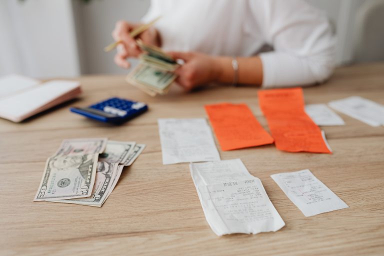 A person using a calculator and cash to plan a household budget. Une personne utilisant une calculatrice et des espèces pour planifier un budget ménager.