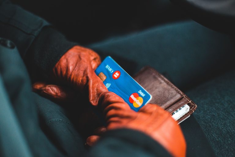 Close-up of hands in gloves holding a credit card and wallet indoors. Gros plan de mains gantées tenant une carte de crédit et un portefeuille à l'intérieur.