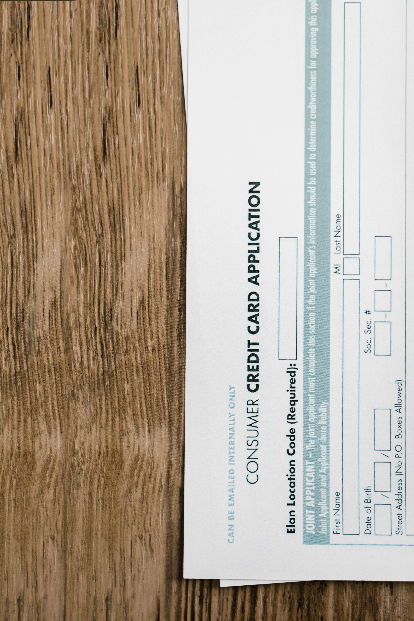 Close-up of a consumer credit card application form on a wooden surface, indicating financial paperwork. Gros plan d'un formulaire de demande de carte de crédit pour consommateurs sur une surface en bois, indiquant des documents financiers.