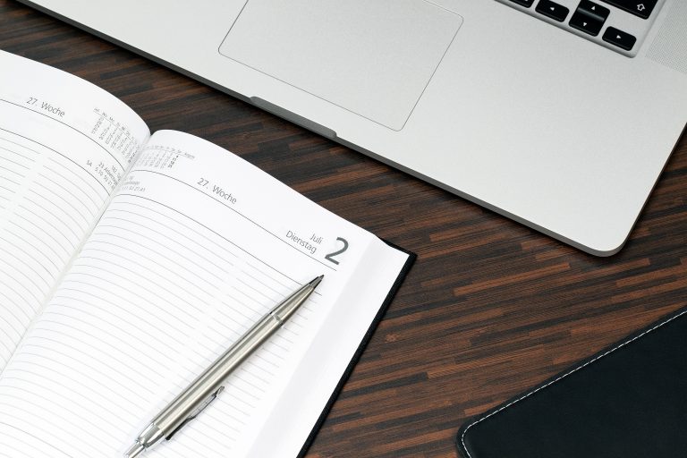 Open planner with a pen and laptop on a wooden desk, ready for organization. Planificateur ouvert avec un stylo et un ordinateur portable sur un bureau en bois, prêt pour l'organisation.