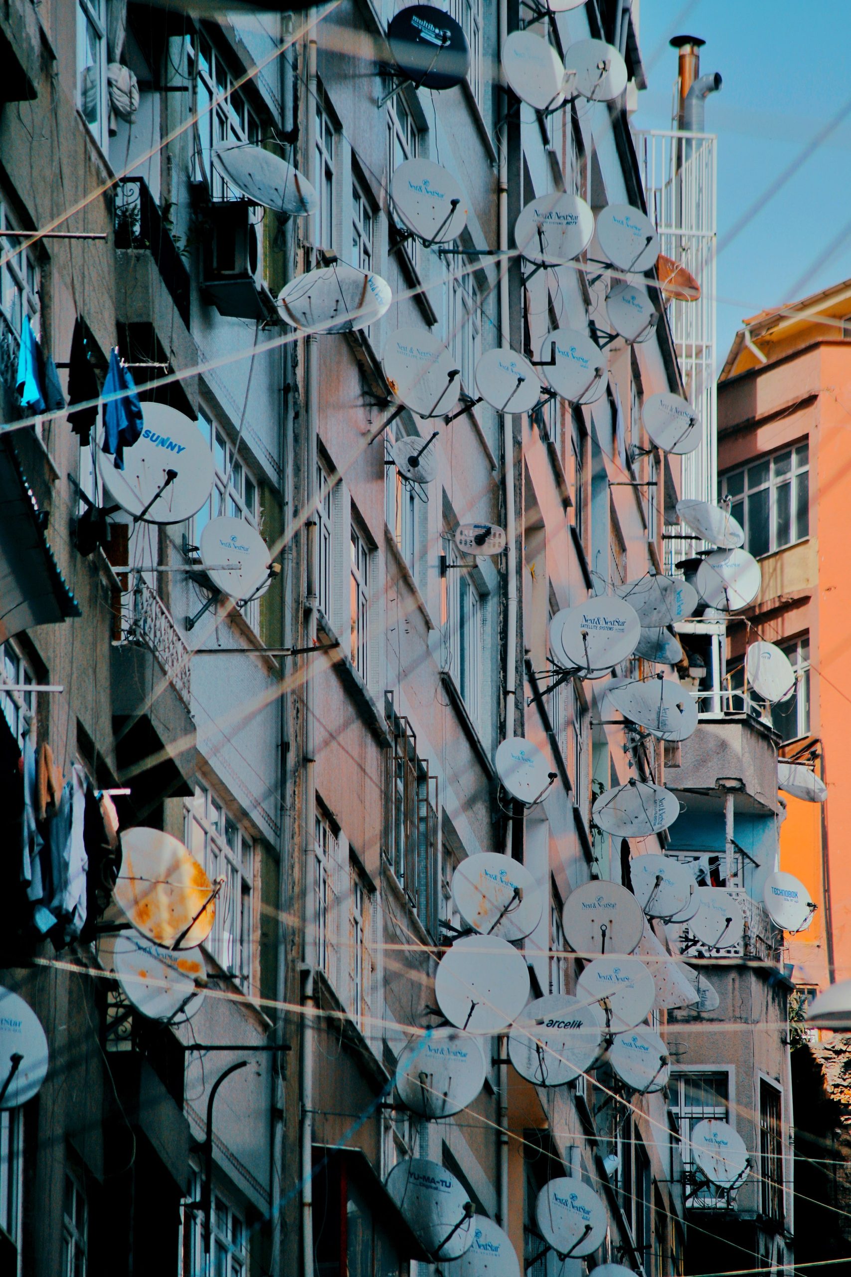 A crowded urban building facade adorned with multiple satellite dishes on a sunny day. Une façade de bâtiment urbain bondée ornée de plusieurs antennes paraboliques par une journée ensoleillée.