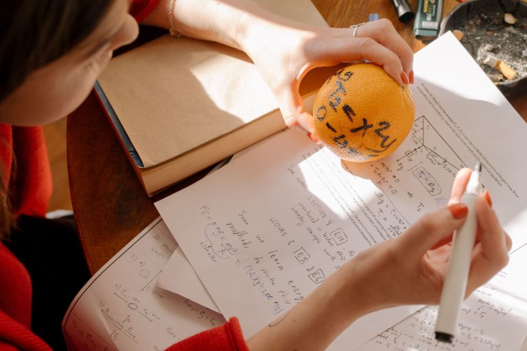 Student studying math creatively using an orange and notes in warm indoor light. Un étudiant étudiant les mathématiques de manière créative en utilisant une orange et des notes à la lumière chaude intérieure.
