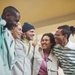 A diverse group of friends smiling and embracing in a warm indoor setting. Un groupe diversifié d'amis souriants et s'embrassant dans un cadre intérieur chaleureux.