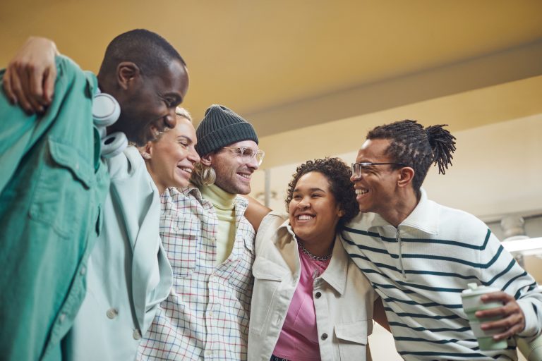 A diverse group of friends smiling and embracing in a warm indoor setting. Un groupe diversifié d'amis souriants et s'embrassant dans un cadre intérieur chaleureux.
