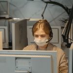 Call center employee wearing mask and headset, focused on computer work. Employée de centre d'appels portant un masque et un casque, concentrée sur le travail informatique.