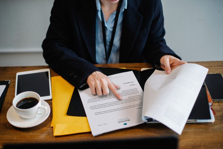 High angle of crop faceless woman in formal wear sitting at wooden table with tablet and coffee and reading documents Vue de haut d'une femme sans visage en tenue formelle assise à une table en bois avec une tablette et un café en train de lire des documents
