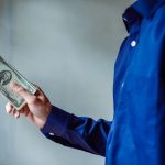 A person in a blue shirt holding a stack of US dollar bills, symbolizing wealth and finance. Une personne en chemise bleue tenant une pile de billets de dollars américains, symbolisant la richesse et les finances.